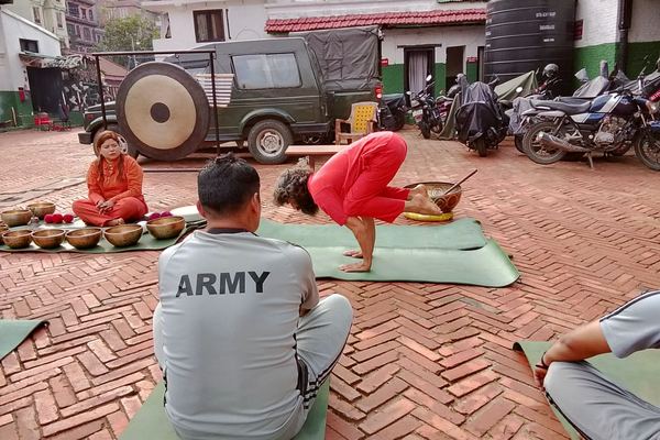 Yogi Ji leading a session in an open barracks yard, a gong and a row of singing bowls set out on mats beside the participants