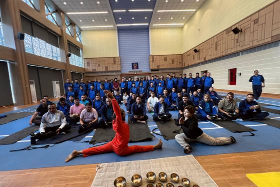 A hall of Nepal Police officers seated in meditation while Yogi Ji leads the session, singing bowls arranged along the floor